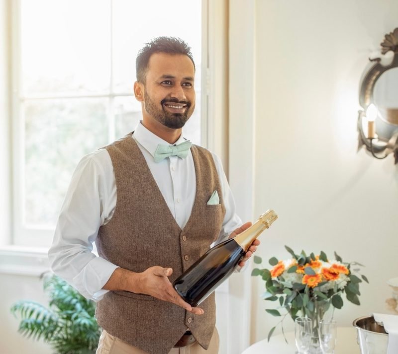 Male,Hotel,Waiter,Holding,Bottle,Of,Sparkling,Wine,Serving,Alcohol