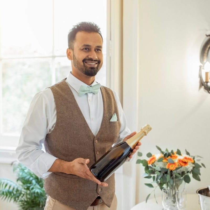 Male,Hotel,Waiter,Holding,Bottle,Of,Sparkling,Wine,Serving,Alcohol